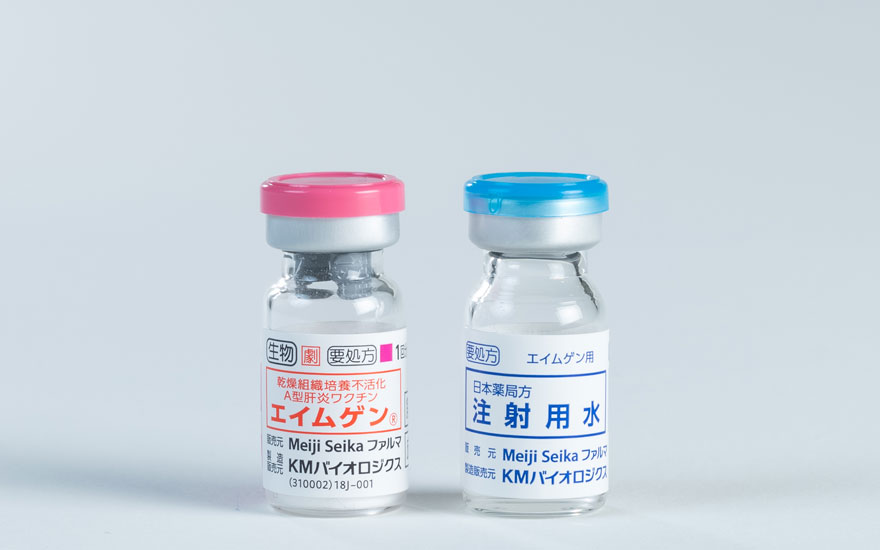 海外渡航時のA型肝炎予防に使用される、KMバイオロジクス社の「乾燥組織培養不活化A型肝炎ワクチン『エイムゲン』」の医薬品パッケージとバイアル瓶・注射用水の製品写真